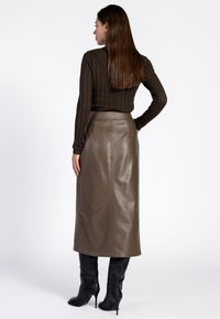 Bruine geribbelde lange mouwtop gecombineerd met een stijlvolle, hoog-getailleerde, metalen bronzen rok. Het model draagt kniehoge zwarte stiletto-laarzen.