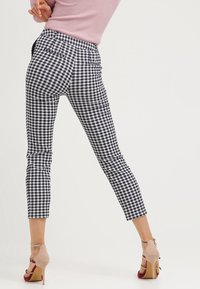 High-waisted, ankle-length pants in black and white gingham fabric with a fitted silhouette and back pockets. Worn with nude heeled sandals.