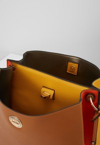Bolso de piel con un exterior marrón, interior amarillo y acentos rojos. Cuenta con un cierre y herrajes dorados, con una textura suave.