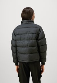 Jachetă puf gri închis cu guler înalt, având un design trapuntat, manșoane elastice și o textură căptușită. Vederea din spate evidențiază volumul și forma sa.