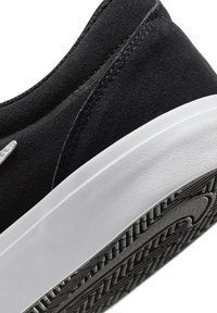 Black suede sneaker with a white rubber sole and textured black outsole. Features subtle stitching and a curved design.