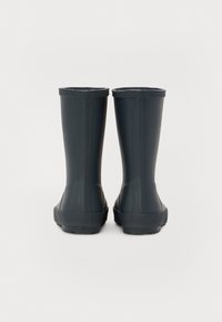 Bottes de pluie en caoutchouc noires avec un design lisse et droit, présentant une légère texture sur le dessus et une semelle extérieure nervurée pour une meilleure adhérence.