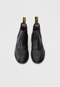 Fekete bőrcipők, slip-on stílusúak, sima felülettel, lekerekített orral és sárga logós húzófülekkel ellátott elasztikus oldalpanellel.