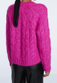 Jasnoróżowy sweter w splocie warkoczowym z ribbowanym obszyciem i teksturowanym wzorem. Charakteryzuje się luźnym krojem i wykonany jest z miękkiej, grubej przędzy.
