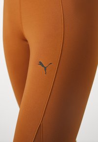 Narancssárga sportleggings, rugalmas anyagból. Fekete Puma logóval és kontrasztos varrással a varratok mentén.
