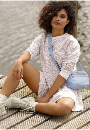 Light pink sweater dress with white zebra stripes, paired with a light blue crossbody bag and beige high-top sneakers, on wooden decking.