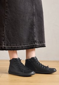 Scarpe alte nere in pelle con una superficie liscia, dotate di lacci e cerniera laterale. Indossate con una lunga gonna di jeans nera.