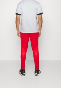 Leggings de sport rouges au design ajusté avec des panneaux texturés contrastants, associés à un tee-shirt gris clair avec des accents noirs.