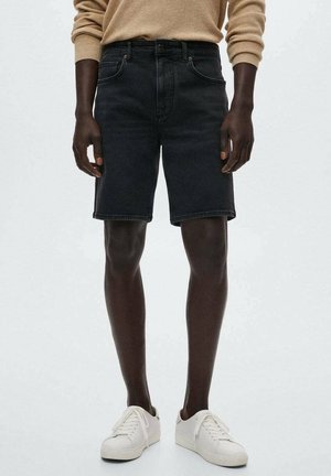 Sorte denimshorts med forlommer, bæltestropper og lige pasform. Sammen med hvide sneakers og en beige sweater. Glat tekstur.