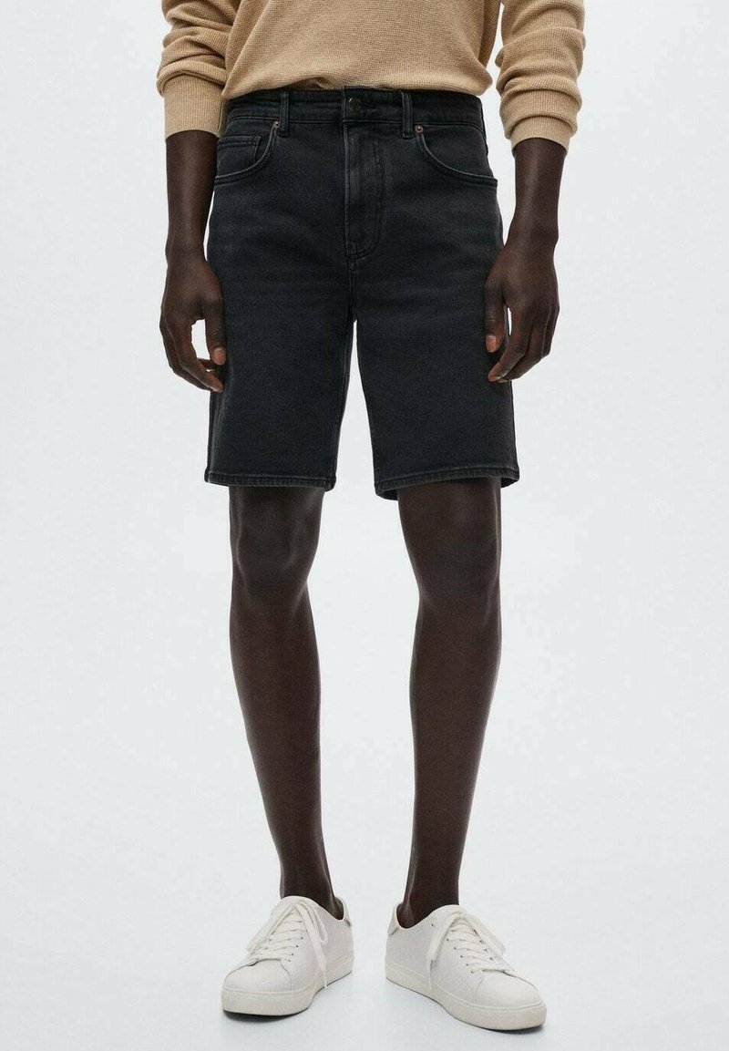 Shorts en denim noir avec poches avant, passants pour ceinture et coupe droite. Associés à des baskets blanches et un pull beige. Texture lisse.