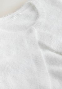 Weißer, flauschiger Cardigan aus weichem Material mit rundem Ausschnitt, Knopfverschluss und dezenten Glitzerelementen.