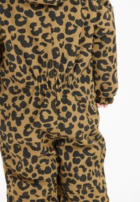 Bagtil af et barn iført en jumpsuit med brune og sorte leopardpletter, der har elastisk talje og manchetter.