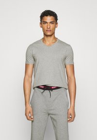Tricou gri cu mânecă scurtă și decolteu în V, confecționat dintr-un material moale, asortat cu pantaloni gri și o curea neagră cu litere roșii.