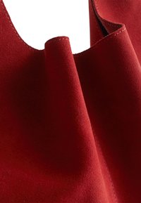 Red suede tote bag featuring a soft texture, smooth edges, and subtle stitching details along the opening and sides.