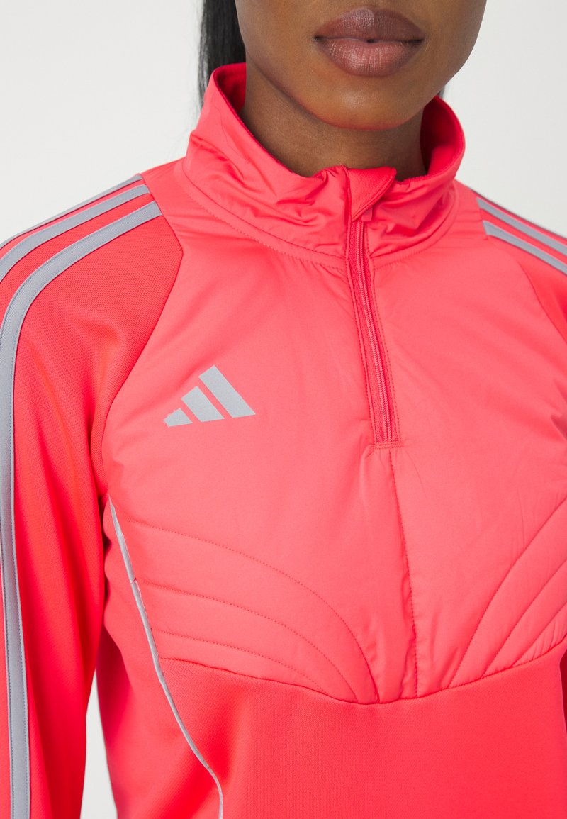 Leuchtend pinkes sportliches Zip-Up-Oberteil mit grauen Schulterstreifen und strukturierten Einsätzen. Das Material wirkt glatt und dehnbar.