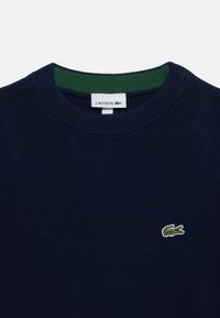 Тъмносин пуловер Lacoste с кръгло деколте с зелен вътрешен илиг и малко зелено крокодилско лого на гърдите.