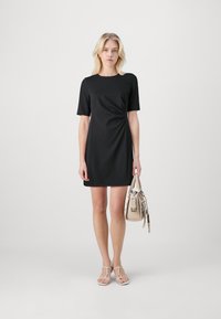 Melnas īsām piedurknēm kleita ar apļa kaklu un savilkumiem sānos. Modelis tur beigu krāsas rokas somu. Gluda auduma, līdz ceļiem.