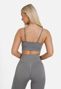 A marca di un reggiseno sportivo grigio con spalline sottili, abbinato a leggings grigi a vita alta con dettagli testurizzati e motivi circolari sul retro.