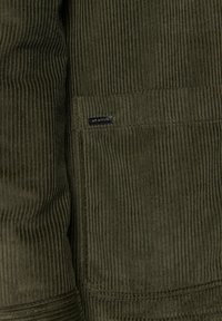 Olive zielony materiał kordowy z wyraźnymi pionowymi prążkami, z wyszywaną kieszenią i małą czarną metką z logo.