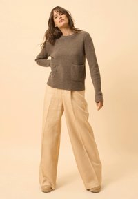 Grauer gerippter Pullover mit zwei Fronttaschen, kombiniert mit weiten, hellbeigen Hosen. Weiche Textur und lässige Passform.