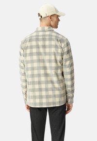 Chemise en flanelle à carreaux beiges et gris, à manches longues, avec des poignets à boutons, texture douce, yoke visible, et ourlet arrondi, montrée de l'arrière.