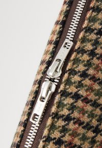 Vlna látka v houndstooth vzore s hnedými, zelenými a červenými odtieňmi, s strieborným kovovým zipsom a hnedou páskou.