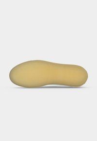 Semelle de chaussure plate beige avec une texture lisse et un léger soutien de la voûte plantaire, présentée sur un fond gris clair uni.