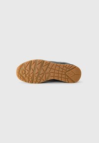 Black sneaker sole featuring a textured rubber design with a patterned tread, showcasing triangular and geometric shapes in a gum color.