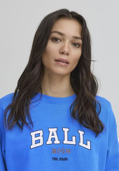 Blå hettegenser med "BALL" i hvite blokkbokstaver, "1974" i oransje, og "THE JEANS" i svart, ribbestrikket rund hals.