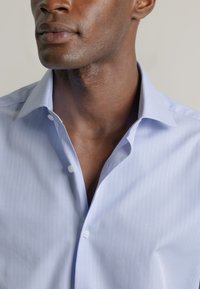Camisa de vestir a rayas azul claro con cuello clásico, que presenta un frente abotonado, un diseño ajustado y una textura suave.