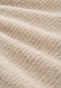 Beige gebreide stof met een geribbelde textuur, die zachte en donzige haptische kwaliteiten toont. Het ontwerp heeft consistente horizontale patronen doorheen.