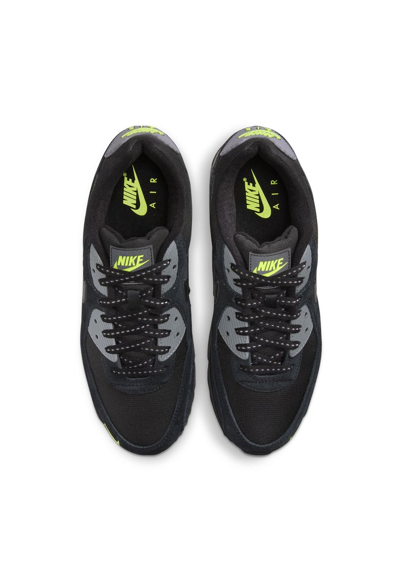Las zapatillas Nike en negro y gris presentan texturas de malla y ante, con un logo y acentos en un brillante verde neón, destacando un diseño clásico con amortiguación de aire.