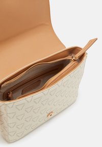 Borsa color crema con motivo a logo. Materiale liscio con chiusura a cerniera, interno beige e una tasca aggiuntiva con zip all'interno.