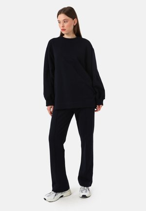 Sweatshirt surdimensionné en bleu marine foncé et pantalon assorti en tissu doux ; associé à des chaussures de sport argentées, d'un design minimal et d'une coupe décontractée.
