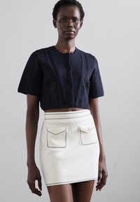 Hæklet navy cropped top med korte ærmer, parret med en hvid mini nederdel med to forlommer og kontrastfarvet sort syning.