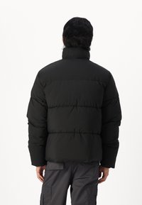 Mustmust värvi pufferjope kõrge kraega, millel on tikand viimistlus, paks isolatsioon ja elastsed mansetid. Kantud hallide cargo-pükste peal.