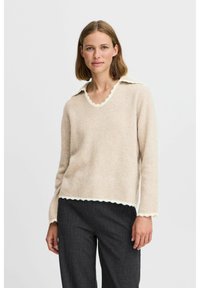 Beige tröja i mjukt material med en scallopad vit krage och nederkant, med långa ärmar och en avslappnad passform. Matchas med mörka byxor.