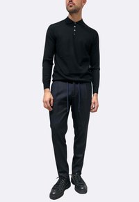 Polo nera a maniche lunghe con una placca a tre bottoni, abbinata a pantaloni blu navy con coulisse e polsini. Il look è completato da sneakers nere.