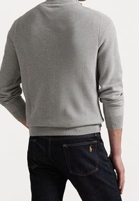 Pull gris en maille avec poignets et ourlet côtelés, associé à un jean en denim foncé avec un petit logo brodé sur la poche arrière.