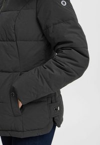 Melna pūkainā jaka ar quilted dizainu, aprīkota ar rāvējslēdzēju, sānu kabatām un pogu akcentiem uz piedurknēm. Gluda, teksturēta auduma.