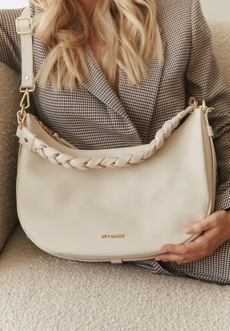 Beige leren schoudertas met een gevlochten schouderriem en gouden hardware, met een gladde textuur en subtiele logo-details aan de voorkant.