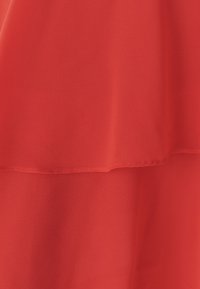 Rode chiffonstof met een zachte, vloeiende textuur, in twee lagen. De randen zijn netjes afgewerkt en licht gerimpeld.