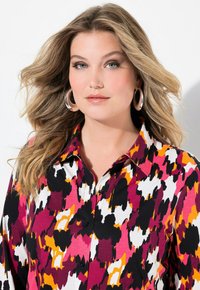 Eine Button-Up-Bluse mit einem mehrfarbigen, abstrakten Muster in Pink, Schwarz, Orange und Weiß, Zierelementen sowie einem Kragen und schwarzen Knöpfen.