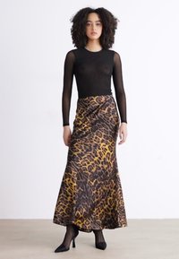 Top de manga larga negro combinado con una falda larga de estampado de leopardo en tonos marrones y dorados, con una textura de tejido suave y fluido.