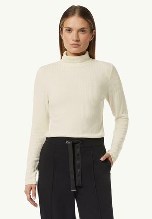 Cream ribbed turtleneck sweater with long sleeves, featuring a slim fit. Paired with black high-waisted pants and a tied waistband detail.