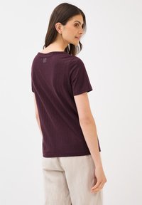 T-shirt à manches courtes, couleur bordeaux, en tissu doux avec une texture subtile, doté d'un col rond et d'une petite impression logo au dos.