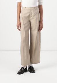 Beige vidde bukser i lett stoff, med flat front, subtile legg og skreddersydd passform. Sammen med svarte loafers.