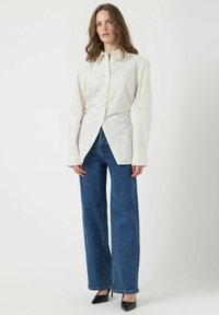 Witte overhemd met lange mouwen, gecombineerd met hoge blauwe denim wijde jeans en zwarte puntige hakken.