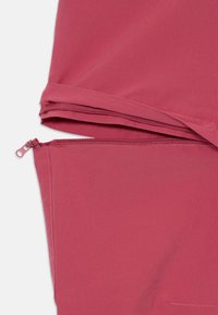 Gros plan sur un tissu rouge montrant une poche zippée à l'ourlet, texture lisse et coutures plates. Conception légère et épurée.