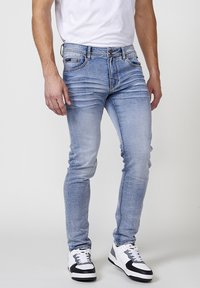 Svetlomodré slim-fit džínsy vyrobené z denimu, s prevarenými detailmi a klasickým dizajnom s piatimi vreckami. V kombinácii s čierno-bielymi teniskami.